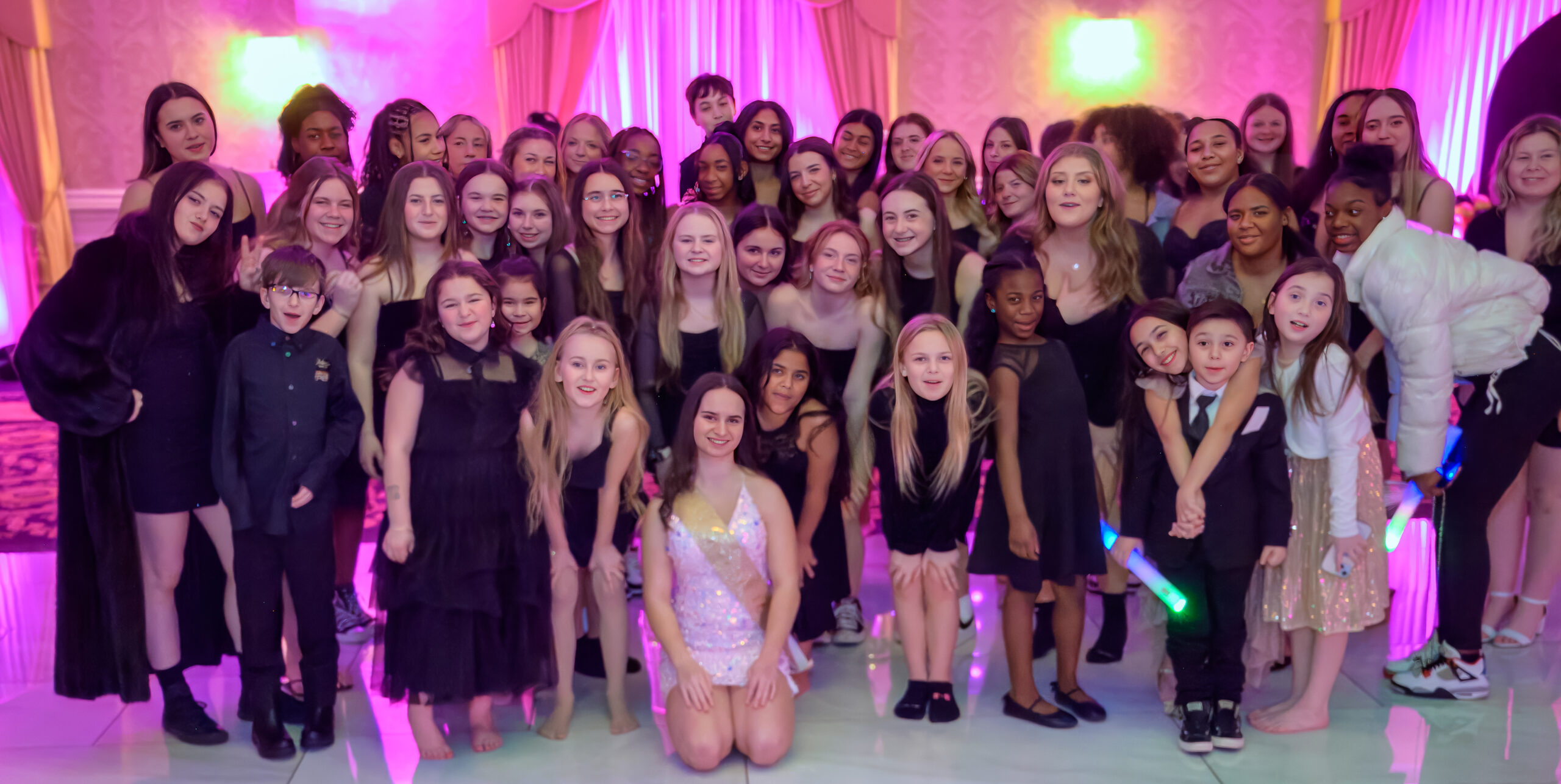 Large group of children and teens posing together at a party with pink/purple lighting.