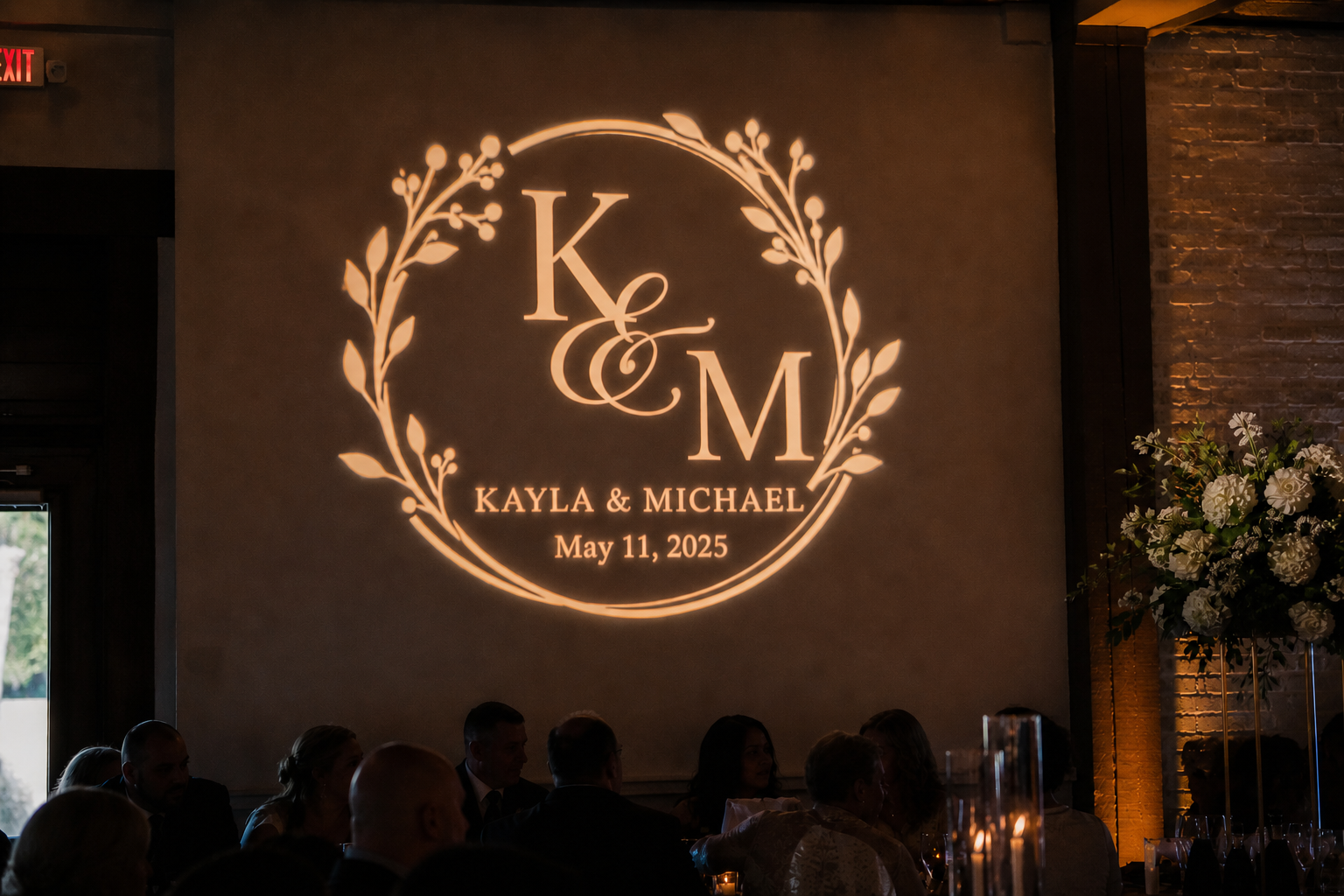 Monogram projection on wall reading K & M, Kayla & Michael, May 11, 2025, with decorative wreath accents.